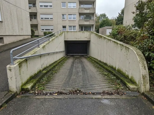 Tiefgaragenzufahrt mit dunklen Belägen und Grünschleier an den Rändern